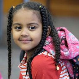 A young student in a classroom smiles for a photo